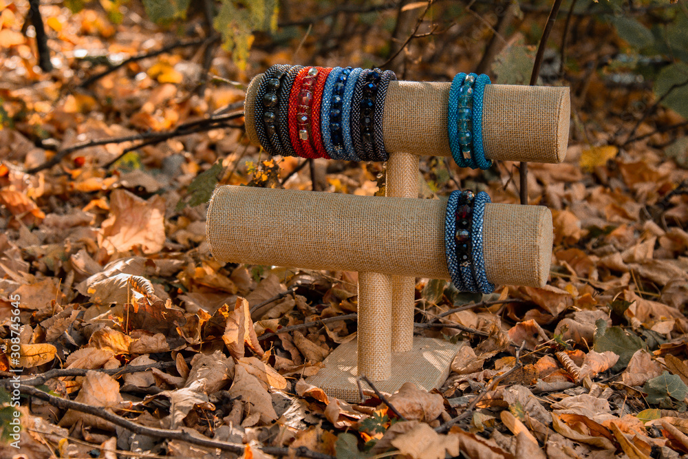 Obraz premium Beautiful, shiny, color bracelet with large beadwork beads. On a special stand for jewelry. Brown autumn foliage on the background.