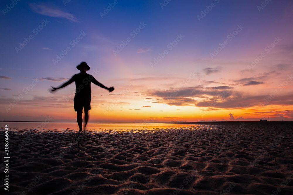 Fototapeta premium Silhouette man on the beach, at sunset. Happy lifestyle in holiday. Freedom life. colorful sky and cloudy view. For web banner