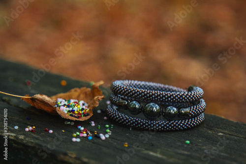 Beautiful, shiny, color bracelet with large beadwork beads. On a special stand for jewelry. Beads are scattered on a wooden table.