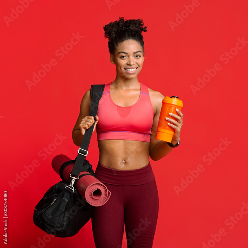 Portrait of happy fitness girl with sporty bag, mat, shaker