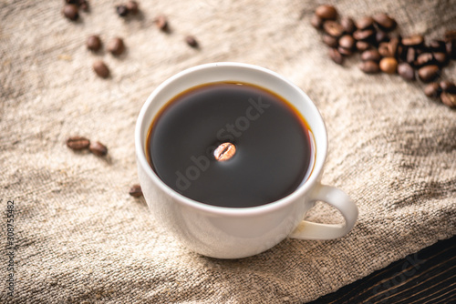 A mug of strong black coffee and scattered grains. Fragrant invigorating drink from freshly roasted coffee beans