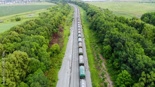 Aerial shot of freight train that travels by rail. Train carries goods and raw materials for heavy industry. Railways are surrounded by trees and endless green fields. Taken by drone at sunset