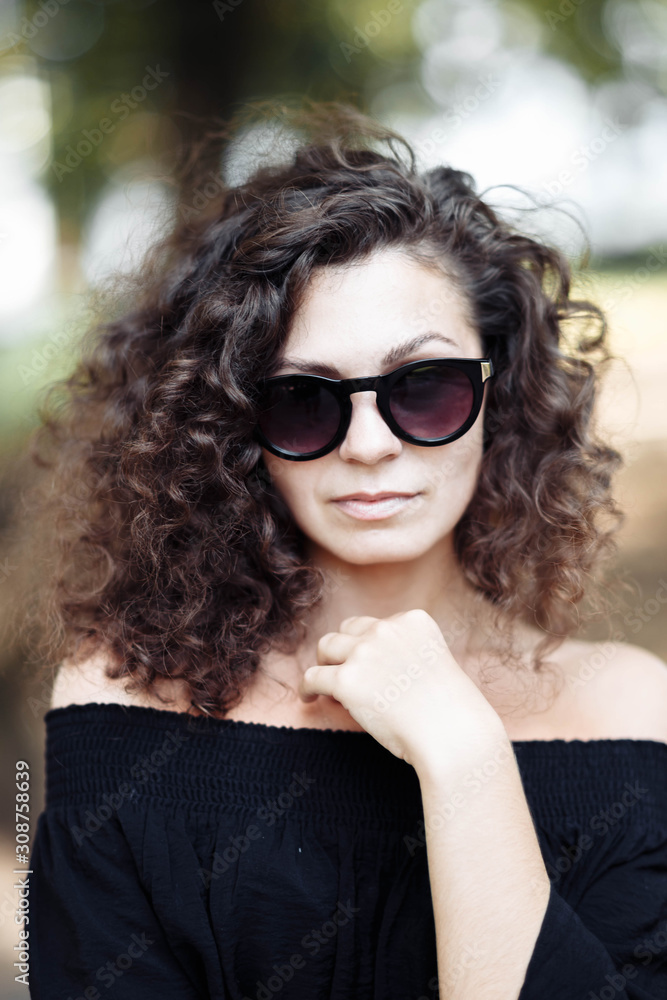 Portrait of a curly young brunette woman in sunglasses on a sunny summer day. Portrait of a curly young brunette woman in sunglasses on a sunny summer day.