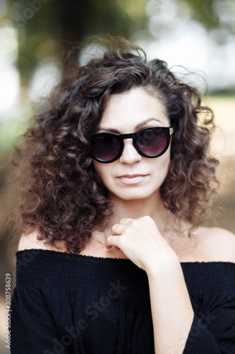 Portrait of a curly young brunette woman in sunglasses on a sunny summer day.