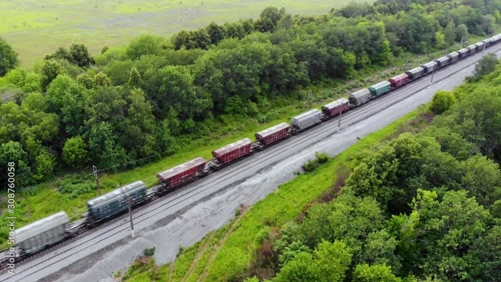 Aerial shot of freight train that travels by rail. Train carries goods and raw materials for heavy industry. Railways are surrounded by trees and endless green fields. Taken by drone at sunset Aerial shot of freight train that travels by rail. Train carries goods and raw materials for heavy industry. Railways are surrounded by trees and endless green fields. Taken by drone at sunset