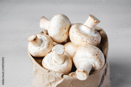 Mushrooms champignons in paper bag on a white wooden table. Close up. Place for text or advertising