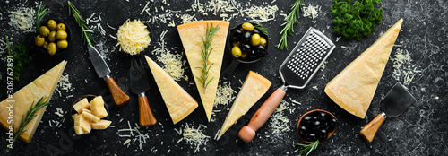Set of hard cheeses with cheese knives on black stone background. Parmesan. Top view. Free space for your text.
