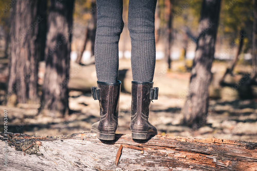 The girls thin legs in rubber boots cross the forest through fallen tree on camping trip. The girls thin legs in rubber boots cross the forest through fallen tree on camping trip.