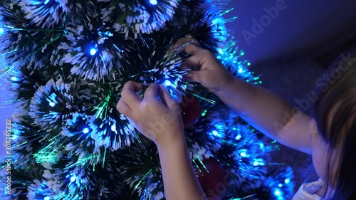 child decorates Christmas tree with Christmas balls. small kid plays by Christmas tree in children's room. daughter examines garland on Christmas tree. happy childhood concept.