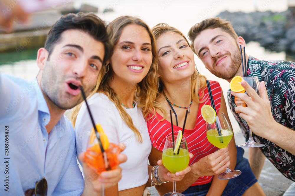 Group of best friends having fun making selfies with smartphone and drinking colorful cocktails at the seaside Group of best friends having fun making selfies with smartphone and drinking colorful cocktails at the seaside