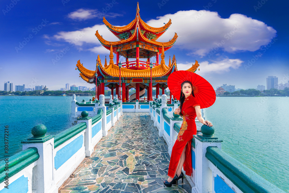 Fototapeta premium Beautiful Asian Chinese Woman Wearing Cheongsam Traditional Red Dress standing on bridge at Wuliting pavilion,Kaohsiung,Taiwan.