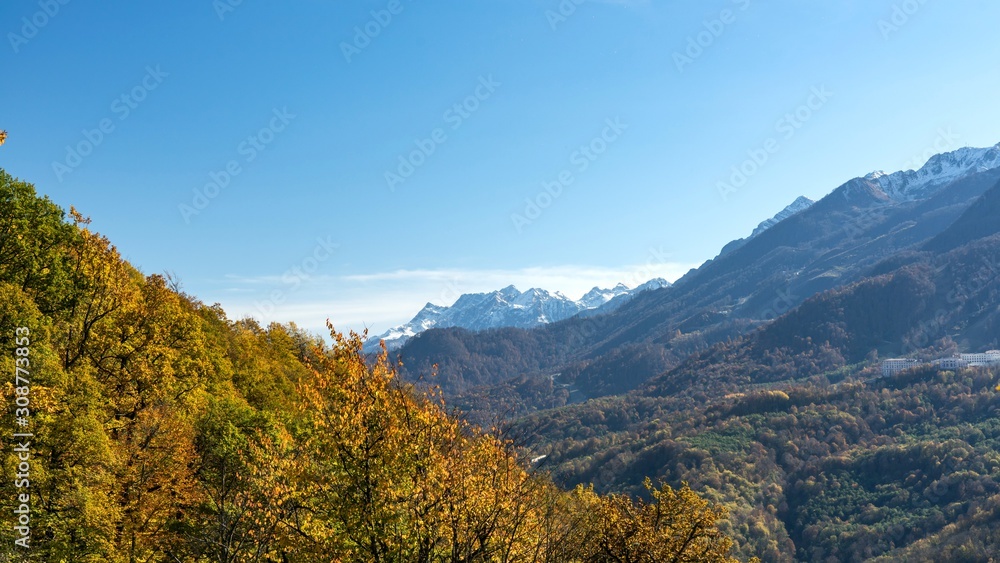 Beautiful autumn forest and mountains covered by snow on background. Krasnaya Polyana, Sochi, Russia.
