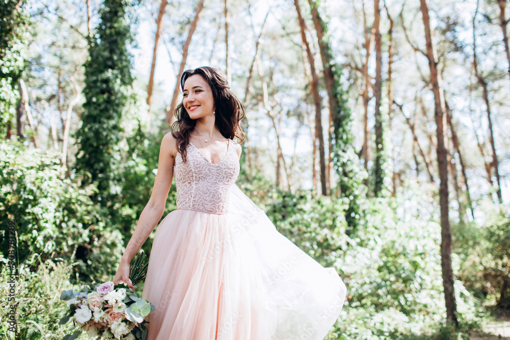 A beautiful bride in a delicate pink dress outdoors. Porter close-up beautiful brunette woman with long dark hair. The girl is holding a bouquet.