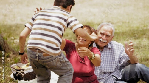 Old people, senior couple, elderly man and woman, husband and wife in park. Outdoors activity, leisure, family recreation. Happy grandfather and grandmother hug grandson, boy, child. Slow motion 
