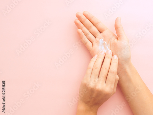 hands applying cream on pink background