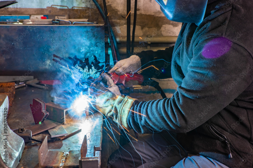 Worker in welding mask at factory. Welding process. Electric welding. Bright yellow sparks. Worker in welding mask at factory. Welding process. Electric welding. Bright yellow sparks.