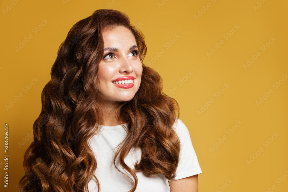 Young pretty model woman with natural makeup and brown curly hair looking up on yellow background. Pretty female smiling Young pretty model woman with natural makeup and brown curly hair looking up on yellow background. Pretty female smiling