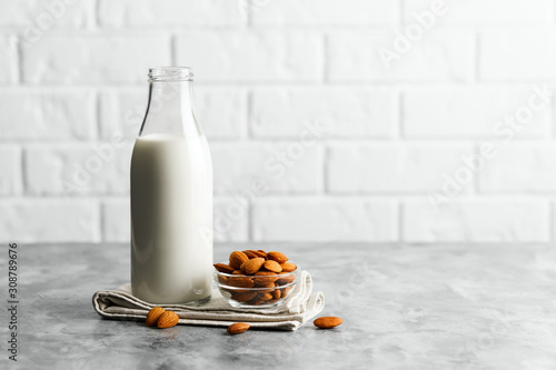 Photos Glass reusable bottle with almond milk and almonds on a marble countertop, kitchen with a white brick wall