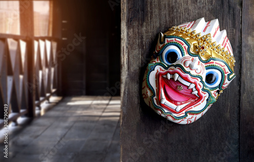 Focus on Thai traditional Hanuman actor's mask hanging on wooden wall with flare light and blurred background of balcony in the old wooden house area, Thai culture and interior architecture concept 