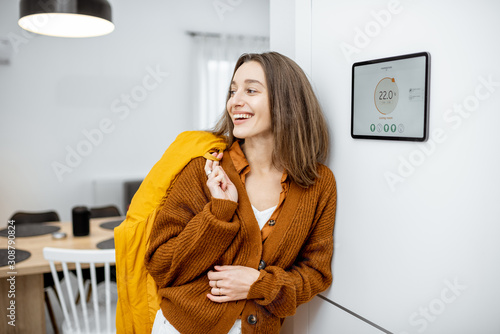 Happy woman feeling warm by coming home. Enjoying smart home remote heating control photo