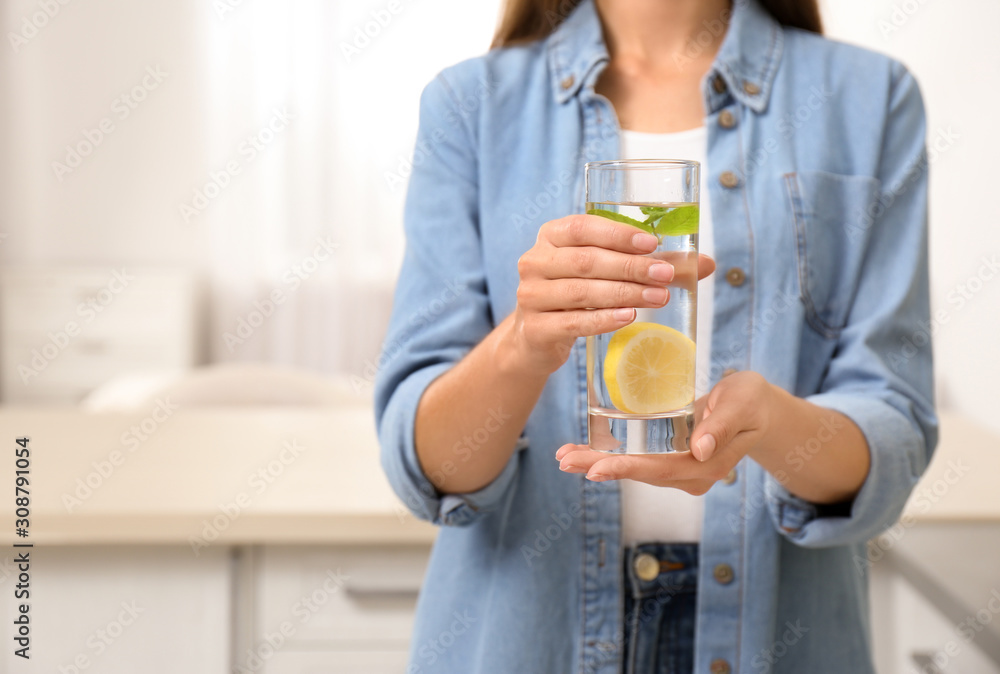 Young woman with glass of lemon water at home, closeup. Space for text