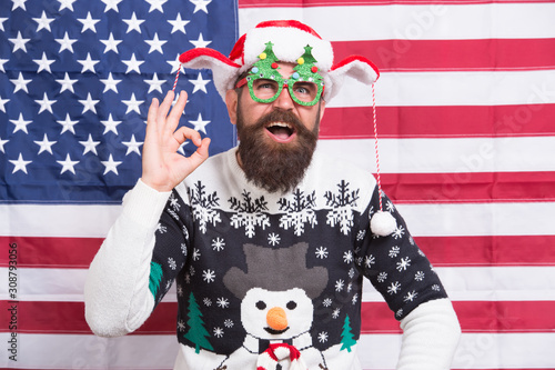 Just perfect. Christmas traditions and observances changed greatly over time. American bearded hipster guy joined cheerful celebration. American tradition. Santa Claus on american flag. Winter season © be free