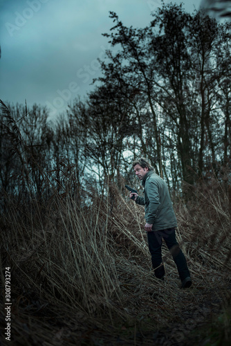 Man with pistol between reed on cloudy day.