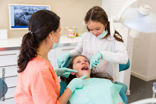 Cheerful female dentist with two little girls  playing assistant and patient