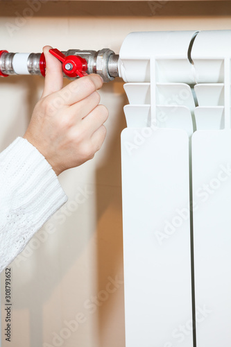 Woman adjusting the red valve of central heating radiator, close up view