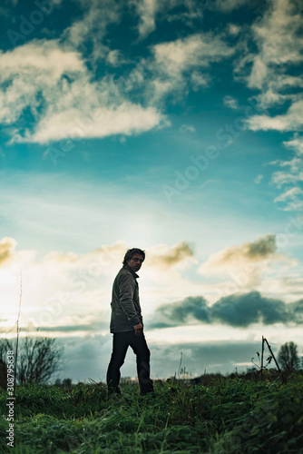 Mysterious man in rural landscape with cloudy sky at sunset. © ysbrandcosijn