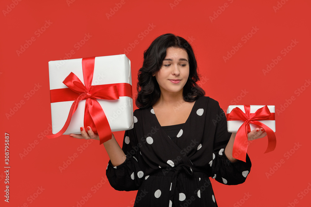 Smiling woman in a black dress choosing between small and big Christmas giftboxes with red ribbon Smiling woman in a black dress choosing between small and big Christmas giftboxes with red ribbon