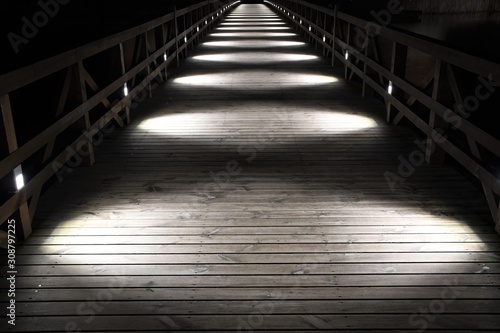 Wooden bridge illuminated by white circular lights at night, perspective 