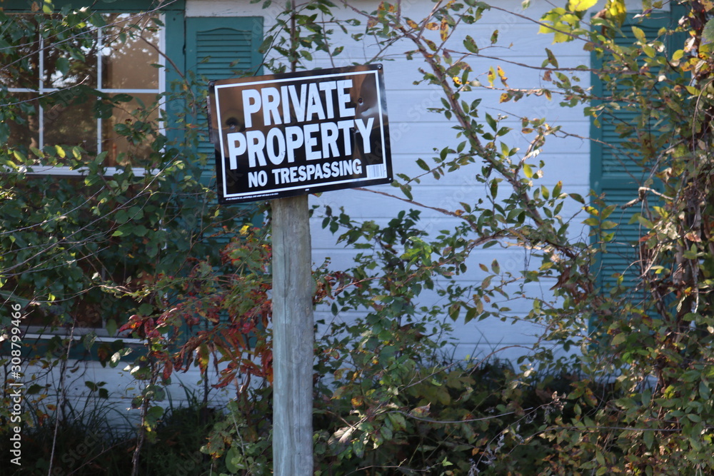 Weathered sign reads Private Property No Trespassing, in front of an abandoned rural country cabin in the woods