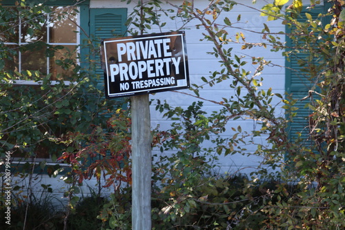 Weathered sign reads Private Property No Trespassing, in front of an abandoned rural country cabin in the woods