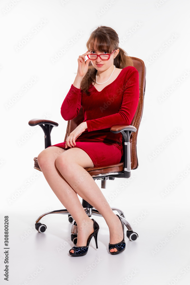 Fototapeta premium Girl in a red dress and red glasses sits in an office chair and straightens glasses