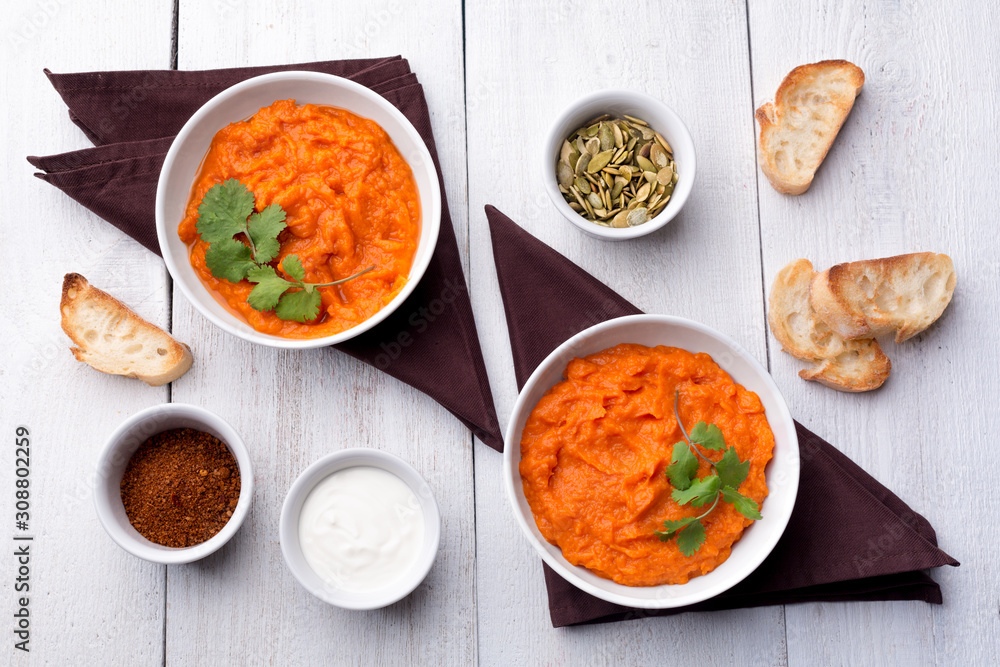 Two plates with a side dish of pumpkin with croutons, sour cream, pumpkin seeds, cilantro and spices on a white wooden background. Two plates with a side dish of pumpkin with croutons, sour cream, pumpkin seeds, cilantro and spices on a white wooden background.