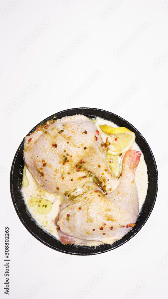 Two fresh chicken legs with spices and lemon in a black pan prepared for frying. Isolated on a white background. Asian and European cuisine. Two fresh chicken legs with spices and lemon in a black pan prepared for frying. Isolated on a white background. Asian and European cuisine.