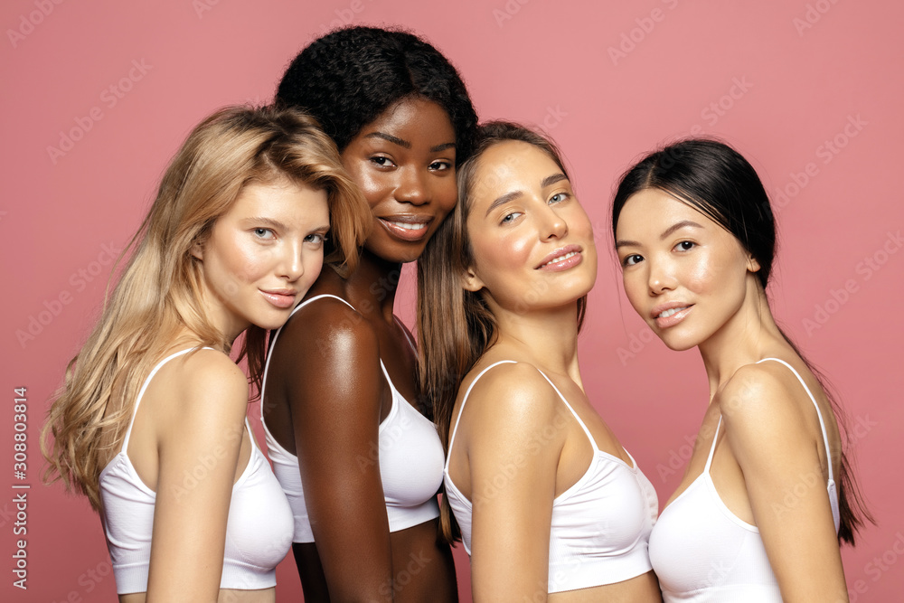 Multi racial Ethnic Group of Womans with diffrent types of skin standing together and looking on camera. Diverse ethnicity women - Caucasian, African and Asian against pink background Multi racial Ethnic Group of Womans with diffrent types of skin standing together and looking on camera. Diverse ethnicity women - Caucasian, African and Asian against pink background