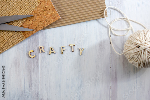 Top view of wooden letters word crafty with thread, cork, cardboard, burlap and scissors over wooden background with copy space 