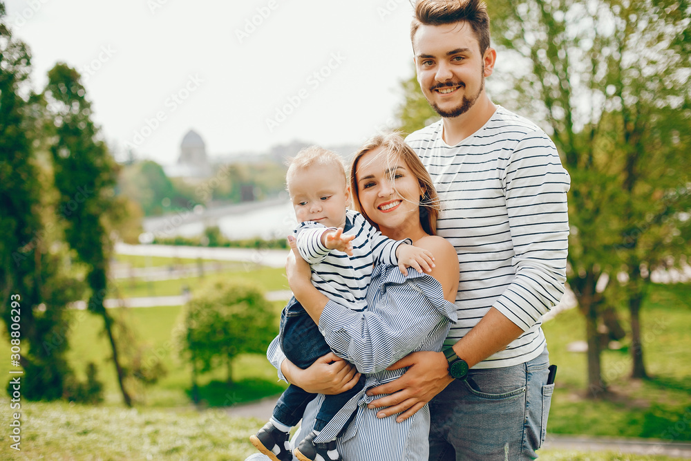Fototapeta premium A young and beautiful blonde mother in a blue dress, along with her handsome man dressed in a white jacket, walks with her little son in the summer solar park
