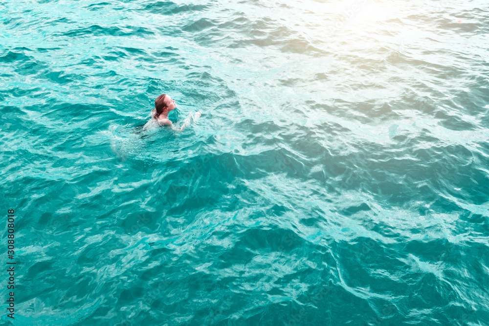 Young woman in blue water, aerial view. Sexy girl relaxing in sea captured from drone. Tropical summer vacation. Tranquility and peace. Person floating on back in ocean. Stock photography.