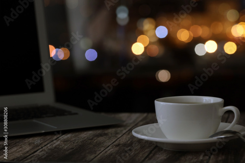 overtime in the evening, work from home, a cup of coffee and a laptop on a night background with beautiful bokeh