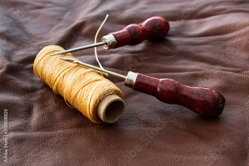 Waxed tread for leather sewing and two puncturing tools on a piece of brown leather. Leather working tools