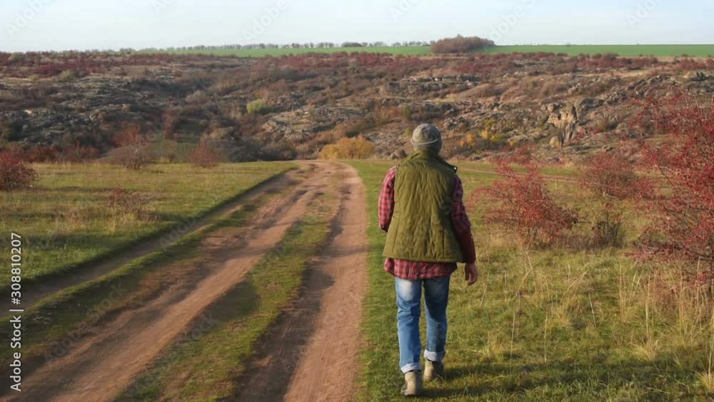 Back view of traveler in plaid shirt walking along the road Back view of traveler in plaid shirt walking along the road