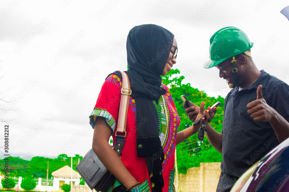 Obraz premium Young African man making a contactless payment with a beautiful woman after fixing a car