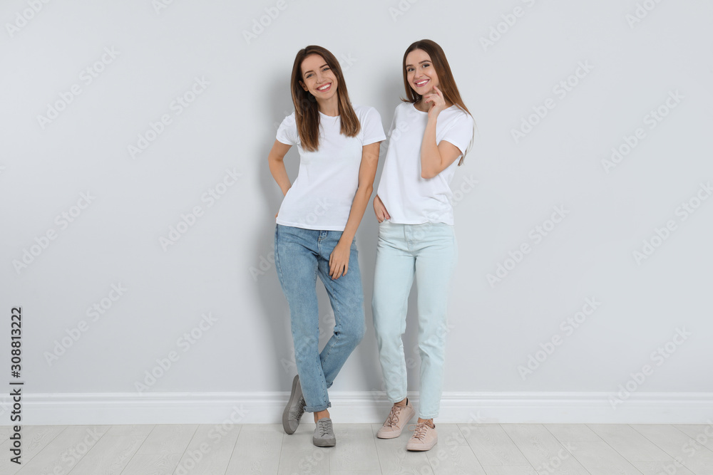 Young women in stylish jeans near light wall Young women in stylish jeans near light wall