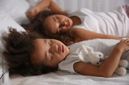Little African-American girl with mother sleeping in bed at night