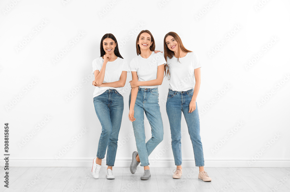 Group of young women in stylish jeans near white wall