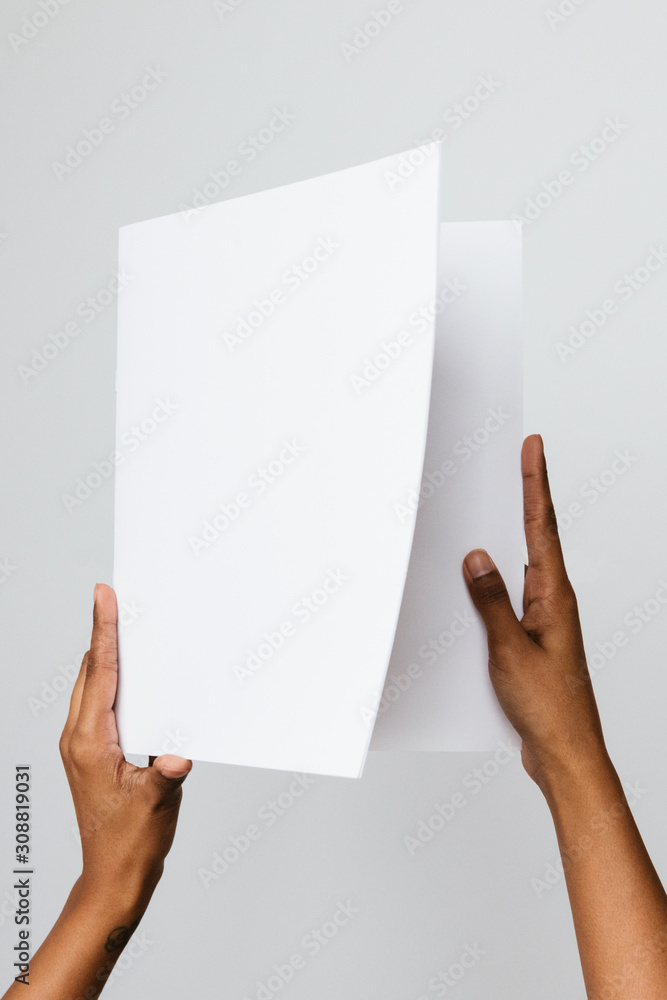 Black, Southeast Asian or ethnic model holding a blank mock-up or dummy of an A5 or half letter-sized brochure or report with both hands. Studio shot on white. Black, Southeast Asian or ethnic model holding a blank mock-up or dummy of an A5 or half letter-sized brochure or report with both hands. Studio shot on white.
