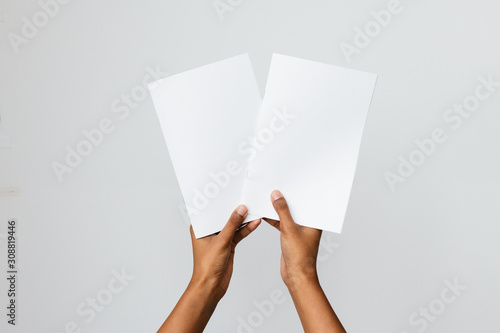 Black, Southeast Asian or ethnic model holding two blank mock-ups or dummies of A4 or letter sized brochures or reports. Studio shot on white. Ideal to place art of two publications for comparison.